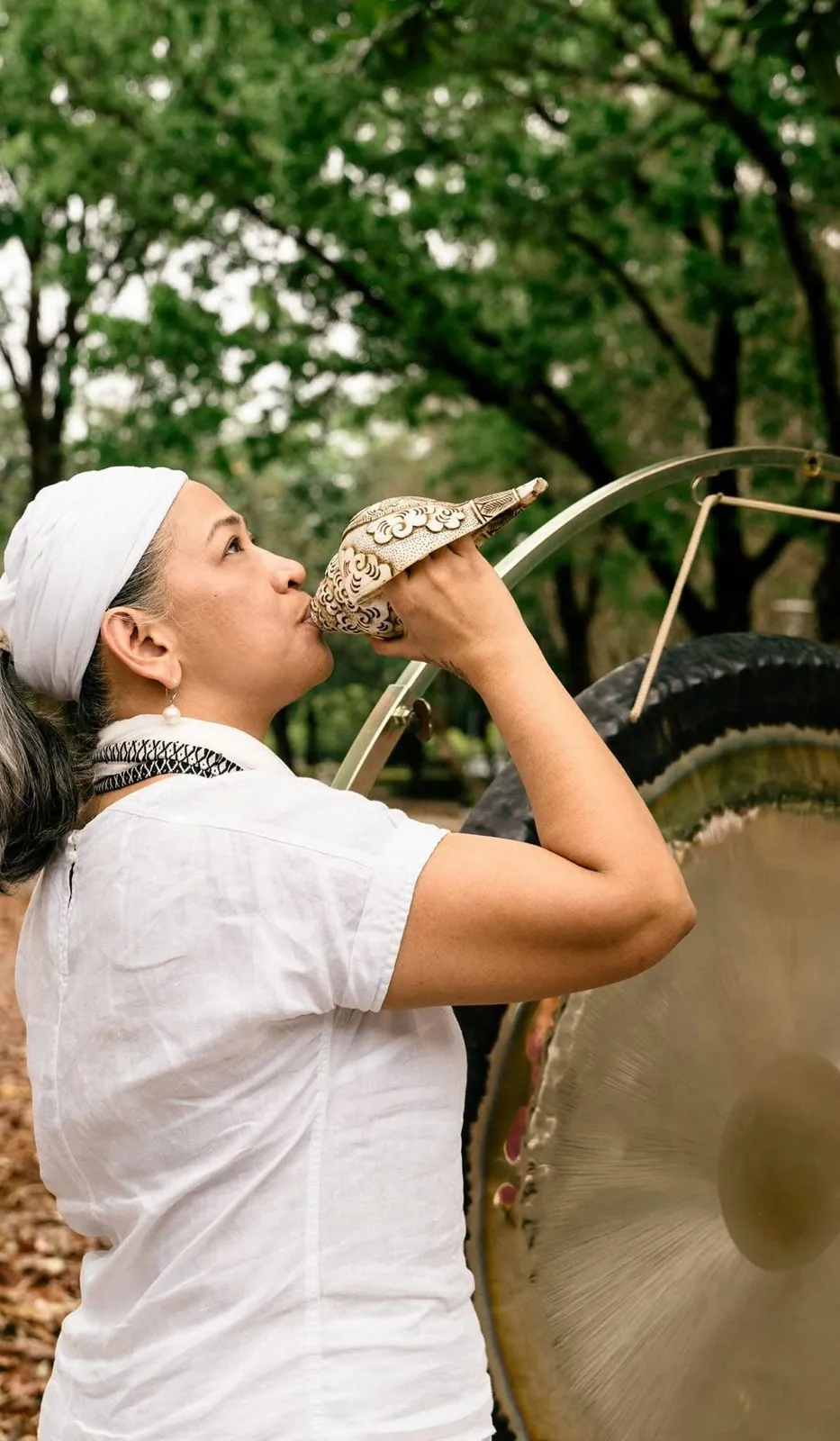 Juariza Aparis sounding a conch shell beside her gong